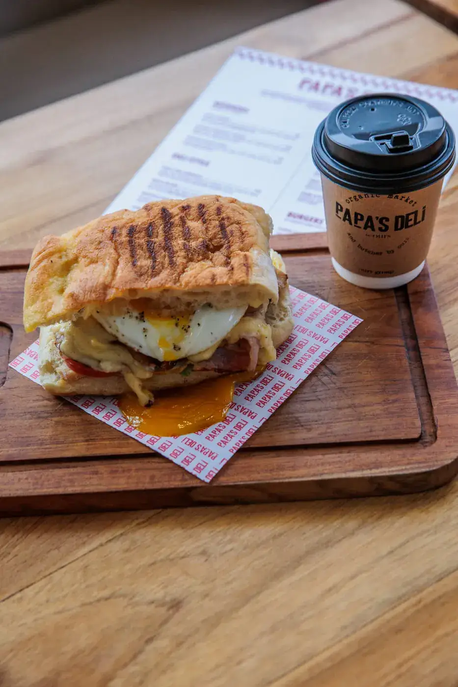Panini panggang dan kopi takeaway di atas talenan kayu