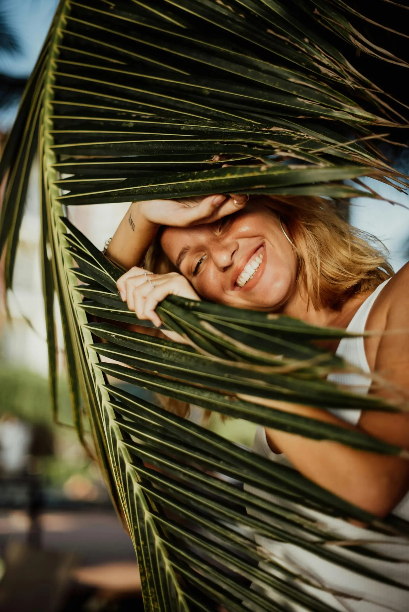 Model swimwear tersenyum di balik daun palem