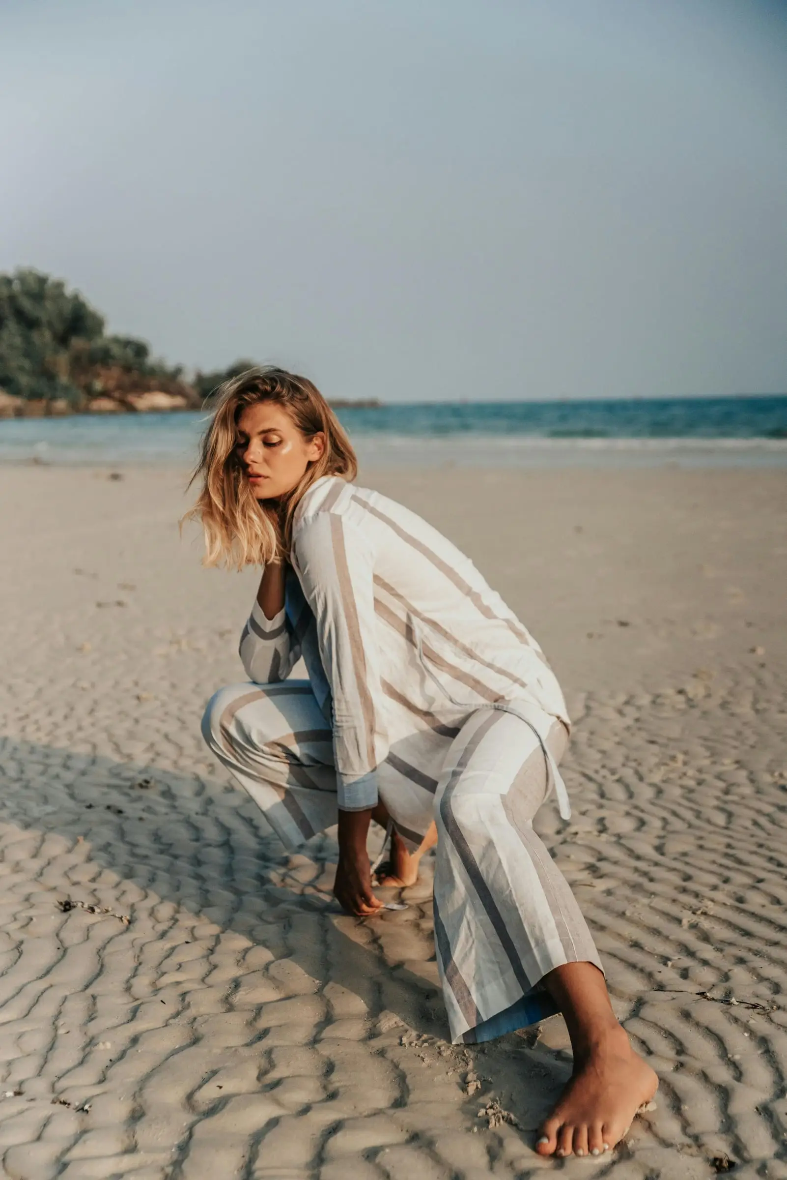 Model berpakaian garis-garis berjongkok di pasir pantai