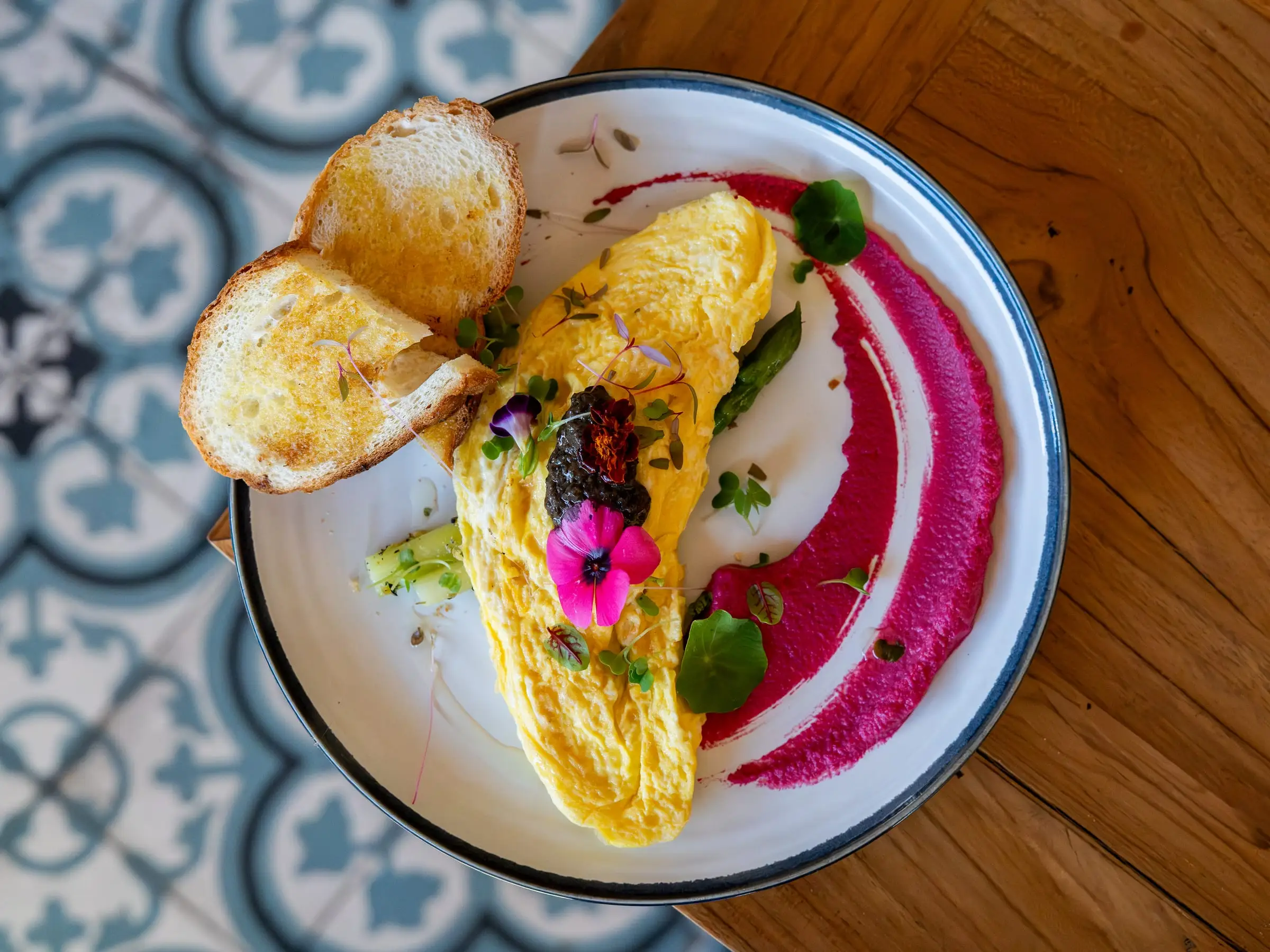 Omelet dengan roti panggang dan saus bit merah muda di atas ubin bermotif