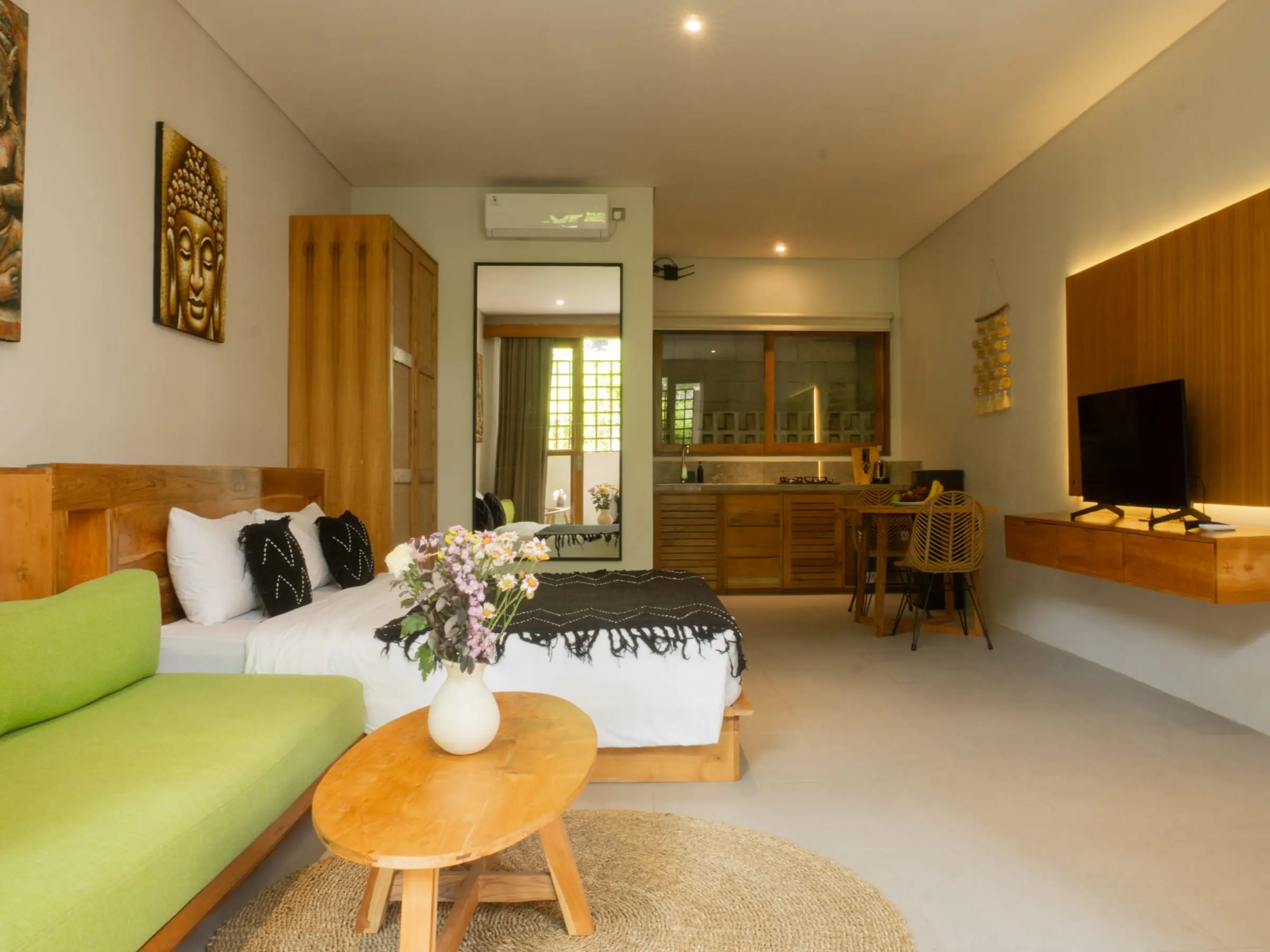 Kamar villa terang dengan sofa hijau, tempat tidur, dan meja kayu