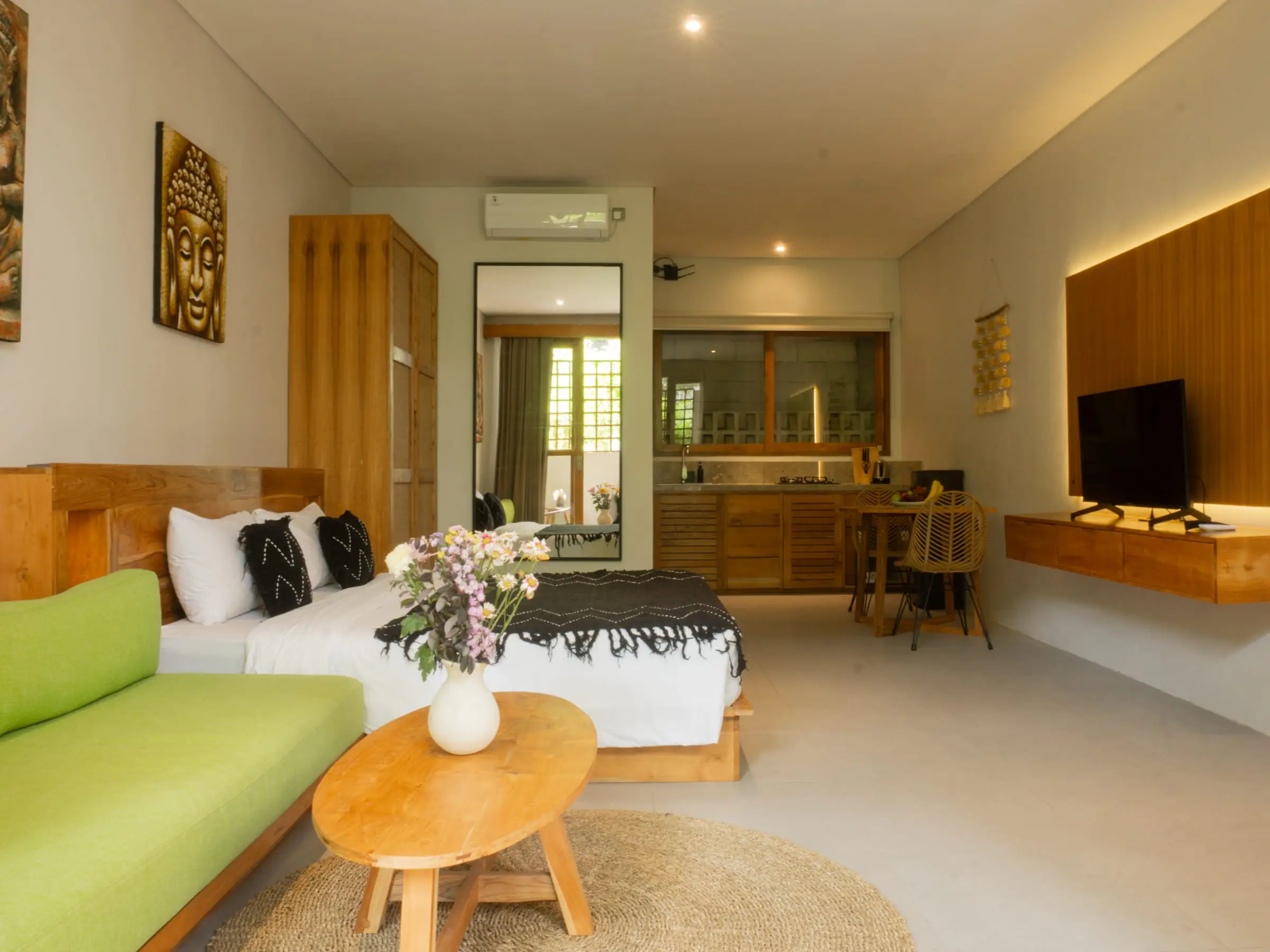 Kamar villa terang dengan sofa hijau, tempat tidur, dan meja kayu