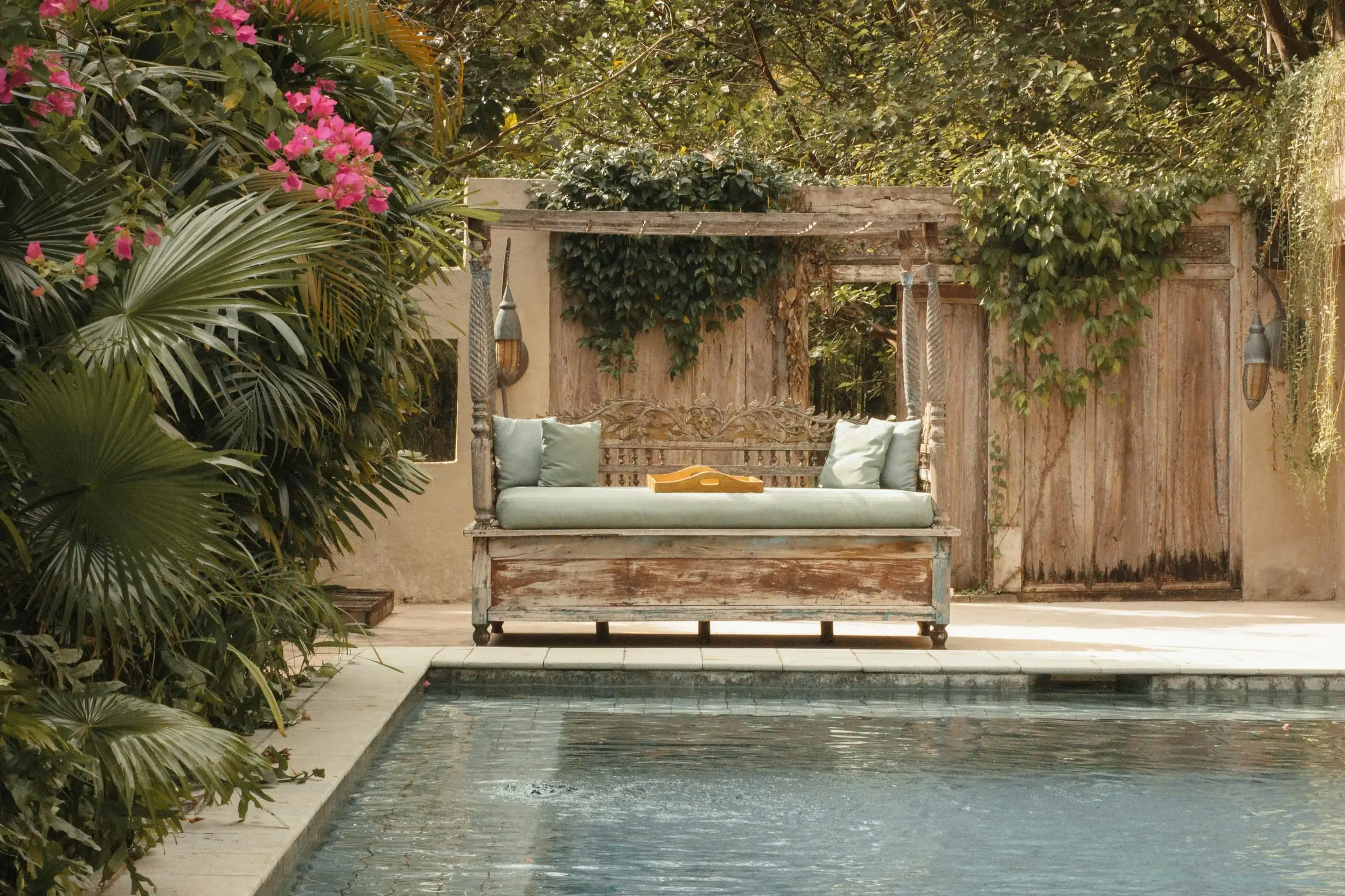 Daybed di gazebo kayu berhias bunga di tepi kolam