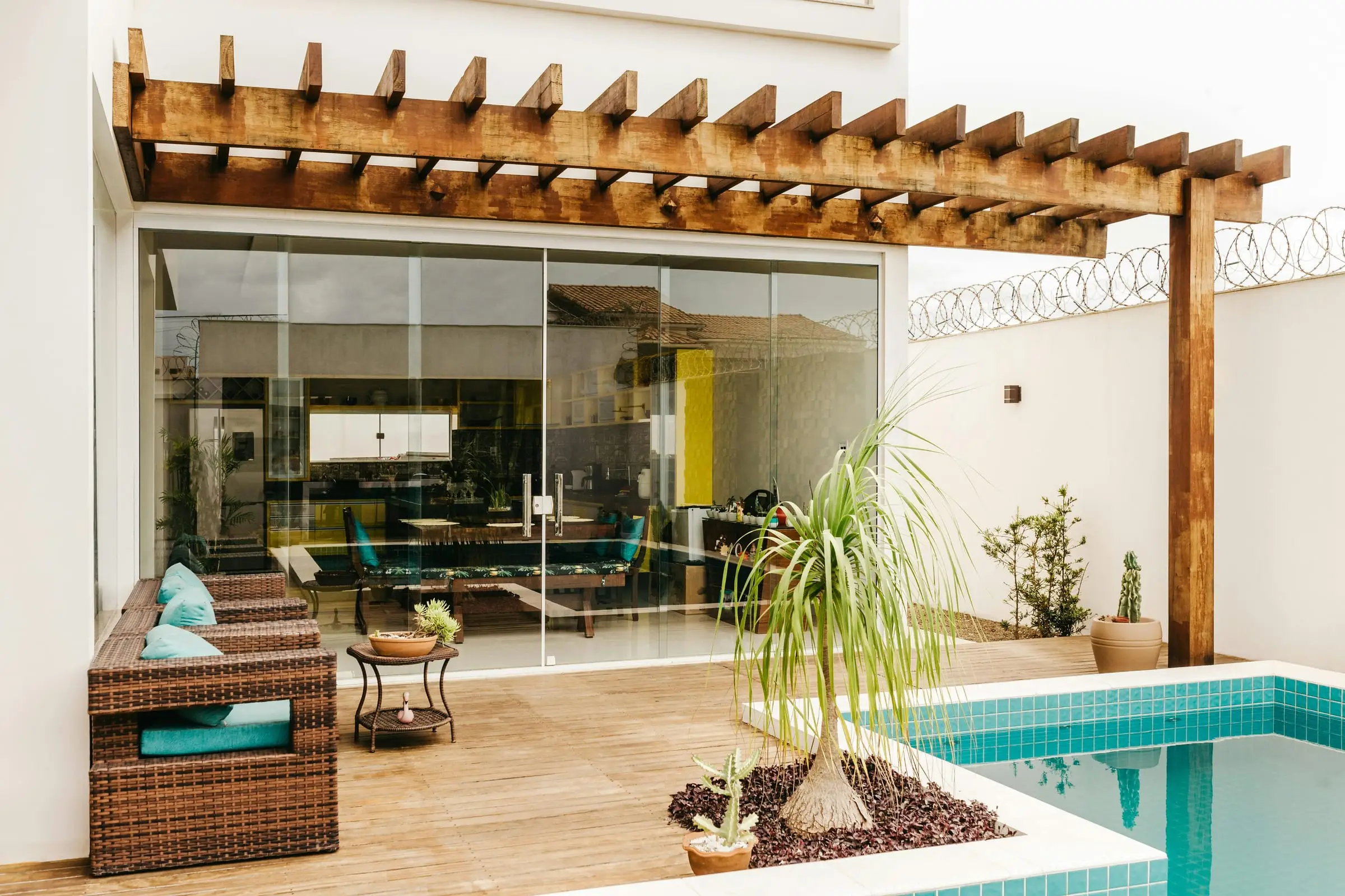 Teras berpergola kayu dengan kolam biru di villa modern